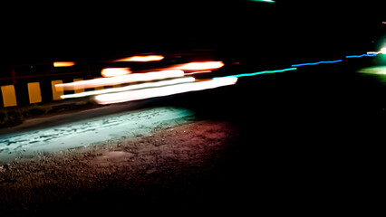 Brightly colored lines of light extend in rapid motion across the dark asphalt, creating a dramatic...