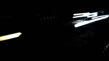 Brightly colored lines of light extend in rapid motion across the dark asphalt, creating a dramatic and abstract time-lapse effect.