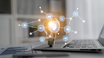 A creative depiction of a light bulb surrounded by digital icons and connections symbolizing ideas and innovation in a modern workspace setting, illustrating technological advancement. Tessel