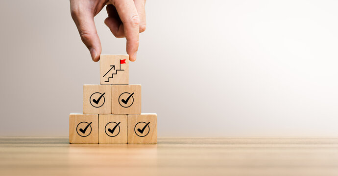 Business growth and success concept with hand placing wooden blocks showing check marks, upward progress symbol. Represents strategy, goal achievement, planning, improvement, and long-term development