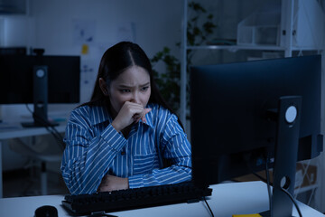 Asian young woman night work looking worried at computer screen in dim office lighting concerned...