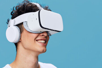 smiling young man wearing virtual reality headset and headphones exploring digital world with blue background, technology and innovation concept