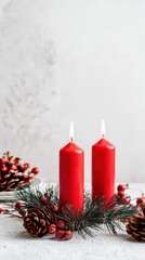 Two red candles are lit on a white background with pine cones and berries