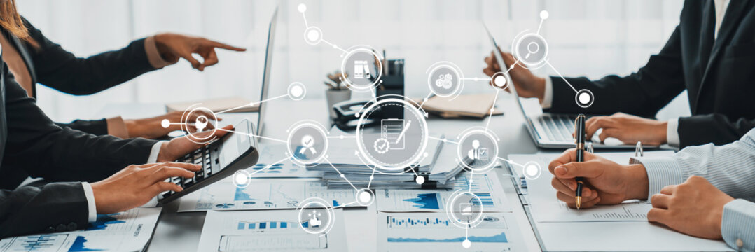 A business team collaborates in a modern workspace with laptops and documents. Digital analytics display data visualization and strategy planning, enhancing productivity and communication. Amity