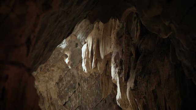 Natural limestone cave texture with stalactites and stalagmites in darkness. Mysterious underground tunnel in Thailand.