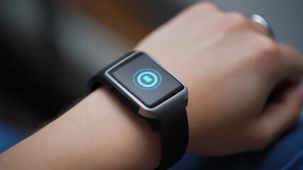 A close-up shot of a person's wrist wearing a modern smartwatch with a glowing blue circular icon on its screen. - Powered by Adobe