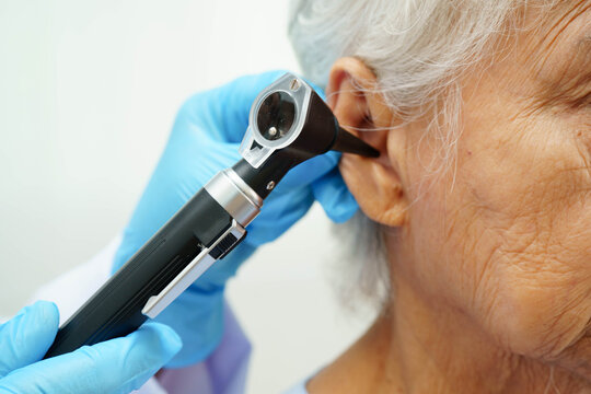 Otolaryngologist or ENT physician doctor examining senior patient ear with otoscope, hearing loss problem. - Powered by Adobe