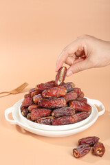 Hand Picking Fresh Medjool Dates from Bowl - Premium Dried Fruits on Beige Background