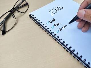 New year 2026 resolution concept. Goal, plan and action written on a notebook with wooden table background. Close up view 