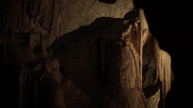 Natural limestone cave texture with stalactites and stalagmites in darkness. Mysterious underground tunnel in Thailand.