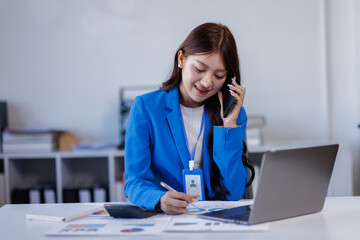 Smiling business woman dressed in white shirt sitting in the office and using tablet computer while talking by her phone.