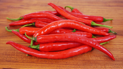 Several fresh red chilies lie on a brown wooden chopping board.