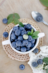 Fresh Organic Blueberries in White Bowl with Green Leaves on Rustic Wicker Placemat