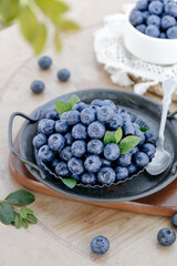 Fresh Organic Blueberries in Rustic Metal Bowl with Green Leaves on Wood Background