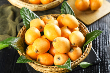 Fresh Loquat Fruits in Wicker Basket with Green Leaves on Wooden Table
