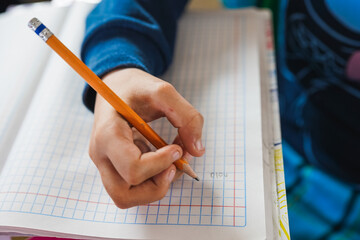Child hand writing in squared notebook with pencil