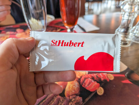 Canada, 08 November 2025 : Hand holding St Hubert moist towelette inside restaurant with food visible
