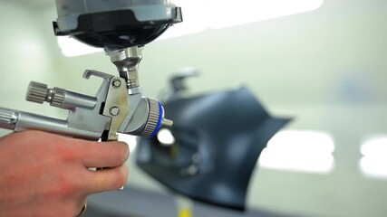Professional auto body technician tests spray gun before painting inside a clean, well lit automotive paint booth. - Powered by Adobe