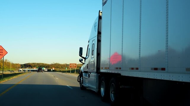 Semi truck hauling cargo along a busy interstate highway on a clear fall day. The trailer moves steadily through traffic, long haul trucking, logistics, supply chain operations