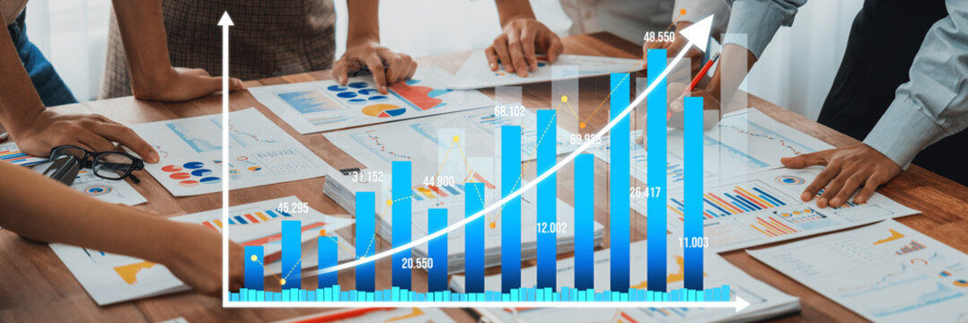 A diverse business team collaborates in a modern office, analyzing a growth chart and various data reports to make informed decisions for future strategies. Amity