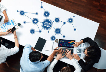 A dynamic business meeting scene featuring professionals engaged in analysis and strategy on a laptop, surrounded by digital icons and data visuals on a modern office table. Amity