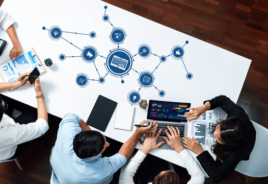 A dynamic business meeting scene featuring professionals engaged in analysis and strategy on a laptop, surrounded by digital icons and data visuals on a modern office table. Amity