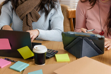 Busy people meet in office, young business team consults on financial work, women collaborate on projects with laptop, tablet, coffee, calculator, and various colored sticky notes across workspace