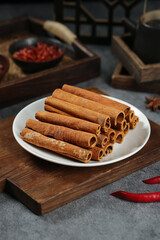 Natural cinnamon sticks on plate with traditional spice grinder and chili peppers in rustic kitchen