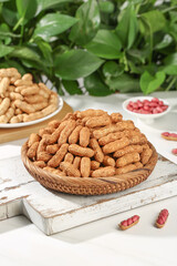 Fresh Raw Peanuts in Shell in Wicker Basket on Rustic White Wood Tray with Green Plants Background