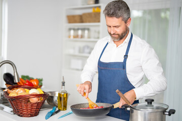 A man chops ingredients for homemade meal in kitchen. A chef preparing a vegetarian dish in the kitchen. A cook with raw vegetables. A man in an apron chops vegetables for a nutritious lunch at home.