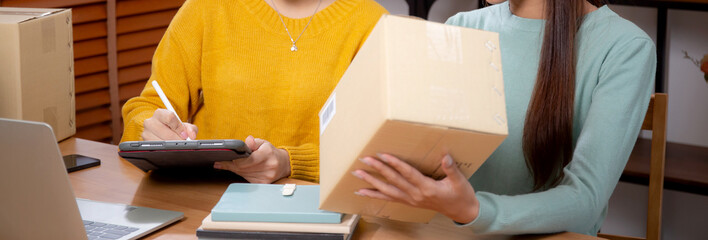 Two young asian woman working while planning online business and checking order with writing on tablet at home, retail with online seller, startup business and cargo, shipping and service.