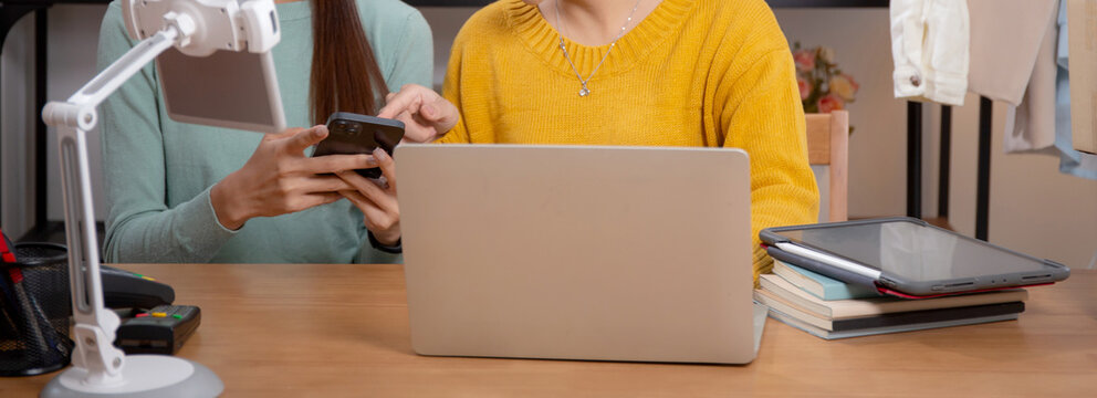 Two young asian woman using tablet and laptop computer for looking review of store in office with success and cheerful, entrepreneur or online seller, ecommerce or startup business, small business.
