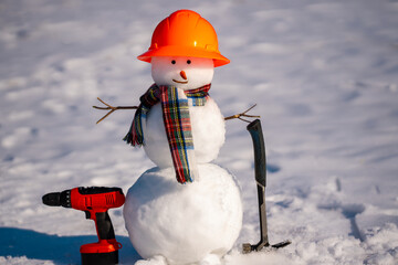 Fototapeta premium Snowman handyman holding saw and hammer. Snow man carpenter. Snowman builder for winter hardware store designs. Snowman construction DIY in winter.