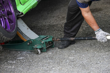 Fototapeta premium Focused mechanic using floor jack to lift custom green car for repair and maintenance. This automotive service shows manual labor involved in vehicle service