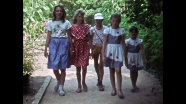 Happy children group walking along path in lush green park during sunny summer holiday. Carefree childhood. Nostalgia child friendship. Kids together in old film. Archival retro 1960s. Vintage archive