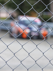 Fototapeta premium Chain link fence barrier on motorsport track, watching race car at high speed. blur of competition creates feeling of intense anticipation from distance