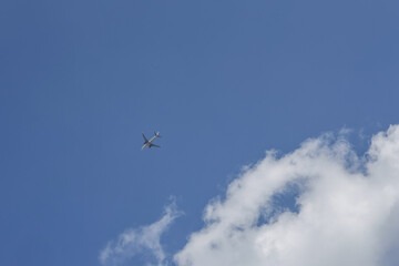 Airplane in flight across vast blue sky with white cloud, peaceful journey representing travel, transportation, and feeling of freedom high in air