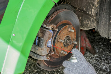Focused mechanic performing brake repair and car maintenance service, spraying lubricant on rusty disc rotor and wheel hub to prevent corrosion and ensure safety