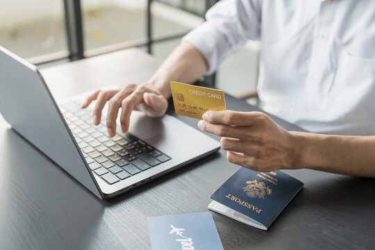 Hand Man Online booking and buying plane tickets using laptop phone and credit card Planning trip travel vacation with passport and ticket