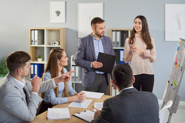 Smiling man and woman standing near whiteboard and explaining ideas to colleagues during team...