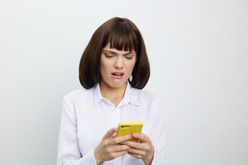 A frustrated woman in a white shirt browses a smartphone, frowning at a screen full of notifications, while standing against a plain light background.