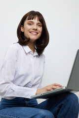 Smiling woman sits indoors with a laptop, casual yet professional, in a clean setting. Soft light highlights focus and technology use for work, study, or creative tasks.