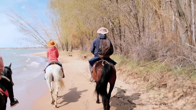 two riders on beach trail with horses walking along shoreline under bright sky, guide in hat leading relaxed pace, sand, gentle waves, windswept trees and warm sunlight creating peaceful vacation vibe