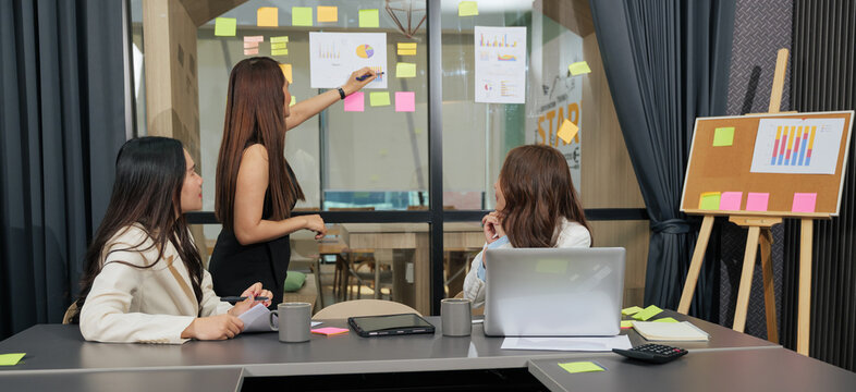 Business women meet, busy team people work on project meeting, analyzing graphs in modern conference room, discussing strategy with visual data presentation