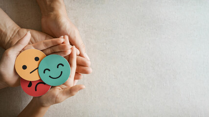 Hands holding sad face hiding behind happy face, bipolar and depression, mental health, split personality, mood change conce