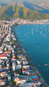 Vertical video. Marmaris, Turkey. Marmaris Bay with yachts, city and beaches at sunset. Complete coastal landscape with urban environment in warm evening light.. Aerial View. Rich colors