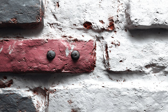 Close-up of a weathered white and red brick wall with two metal rivets.