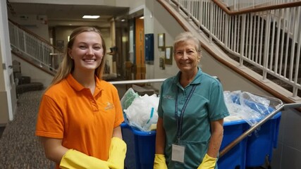 Cheerful Custodians: Two women, dressed in work attire and gloves, standing confidently in a clean, well-lit interior, representing dedication and diligent services.