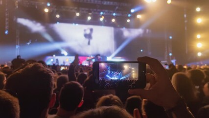 Concert crowd with phone recording the show, stage lights in background.