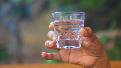Hand holding a glass of clear water in a natural setting